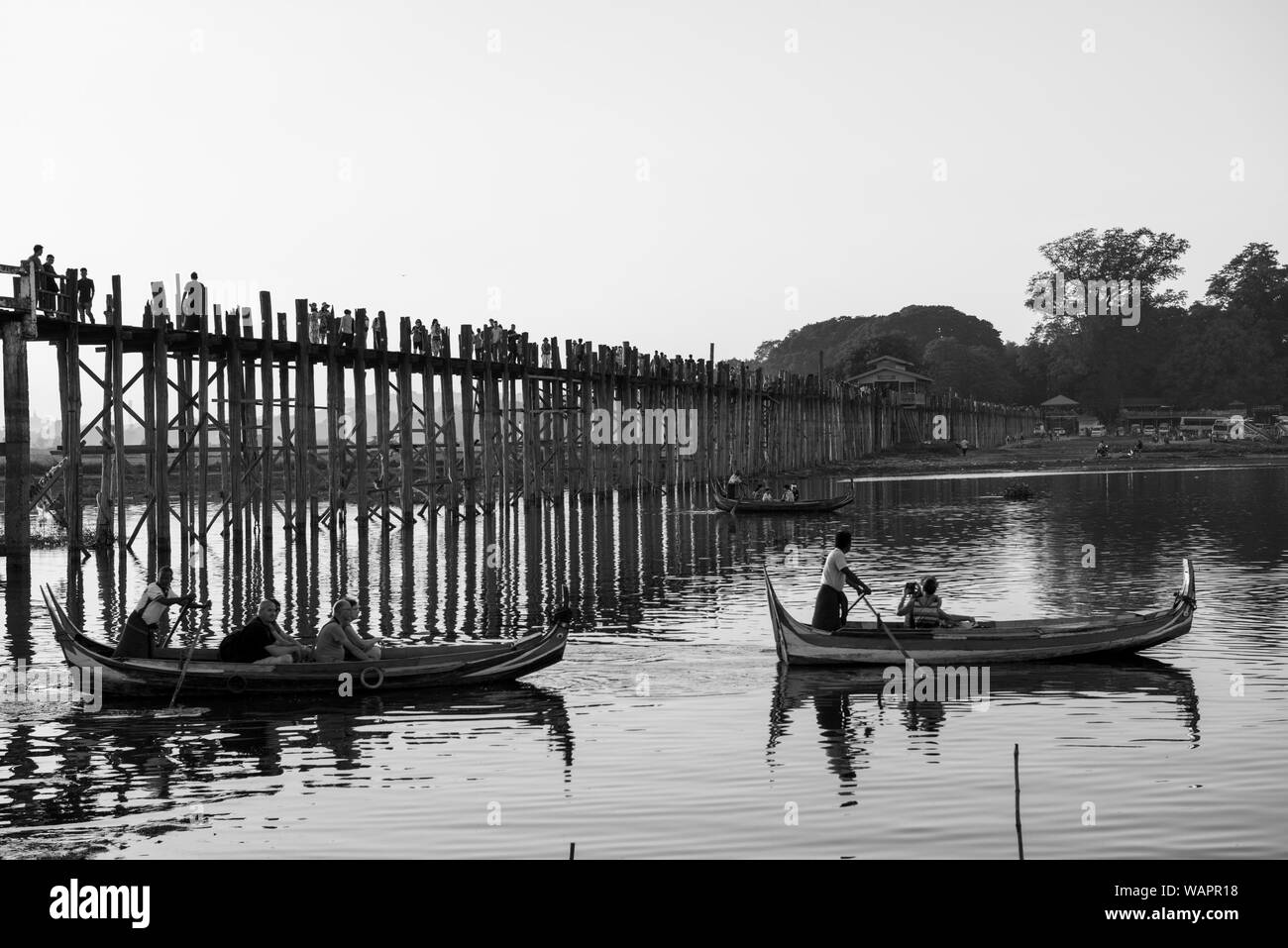 MANDALAY, MYANMAR - 03 décembre, 2018 : Noir et blanc photo de U Bein Bridge et tour en bateau touristique pendant le coucher du soleil à Mandalay, Myanmar Banque D'Images