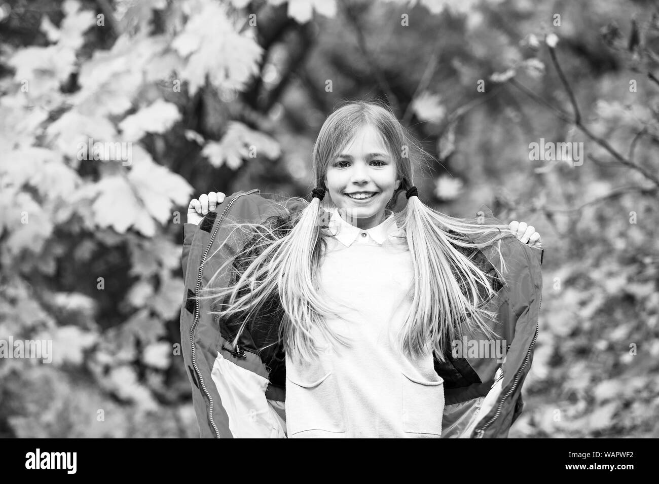 Fille avec capuche manteau usure automne profitez de la nature. Manteau pour porter l'enfant saison d'automne. Vêtements d'automne et de la mode concept. De longs cheveux blonds de l'enfant parc automne marche arrière-plan. Se sentir confortable en veste chaude. Banque D'Images