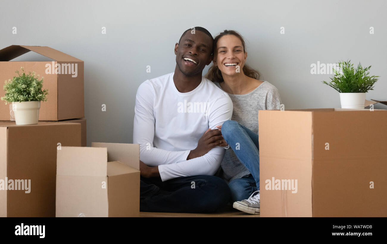 L'origine ethnique mixte heureux couple looking at camera s'asseoir avec des cases Banque D'Images
