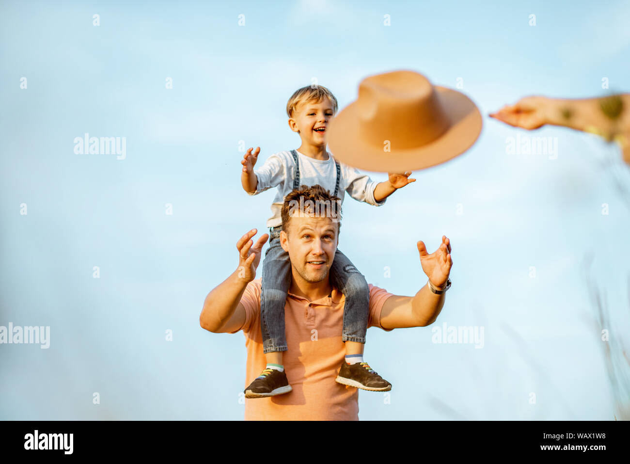 Portrait d'un père heureux avec mon jeune fils à cheval sur les épaules, playign avec chapeau sur le fond de ciel bleu à l'extérieur. Concept d'une famille heureuse sur Banque D'Images