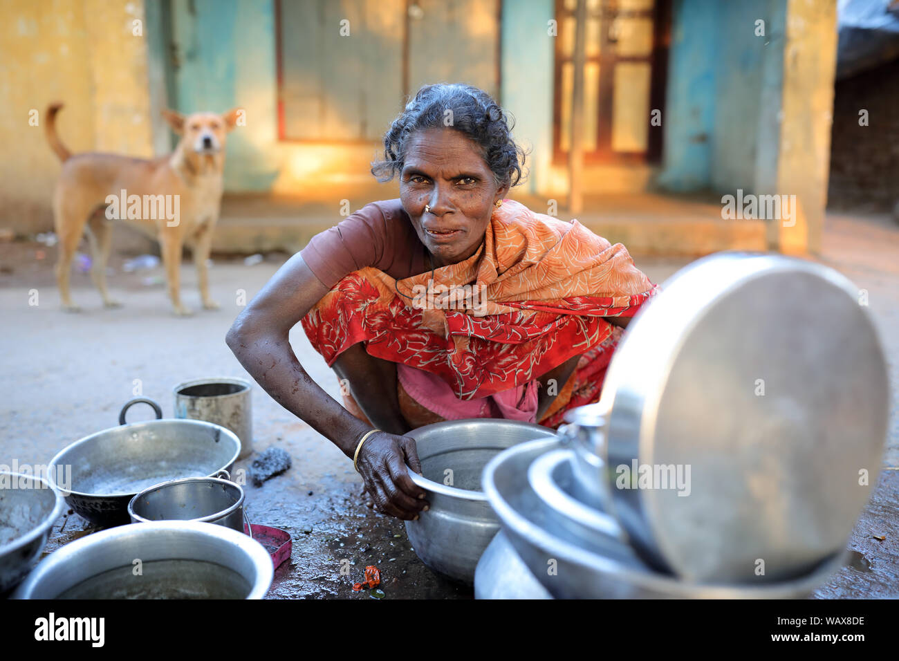 Une vieille femme nettoie la vaisselle dans les rues de Madurai, en Inde. Banque D'Images