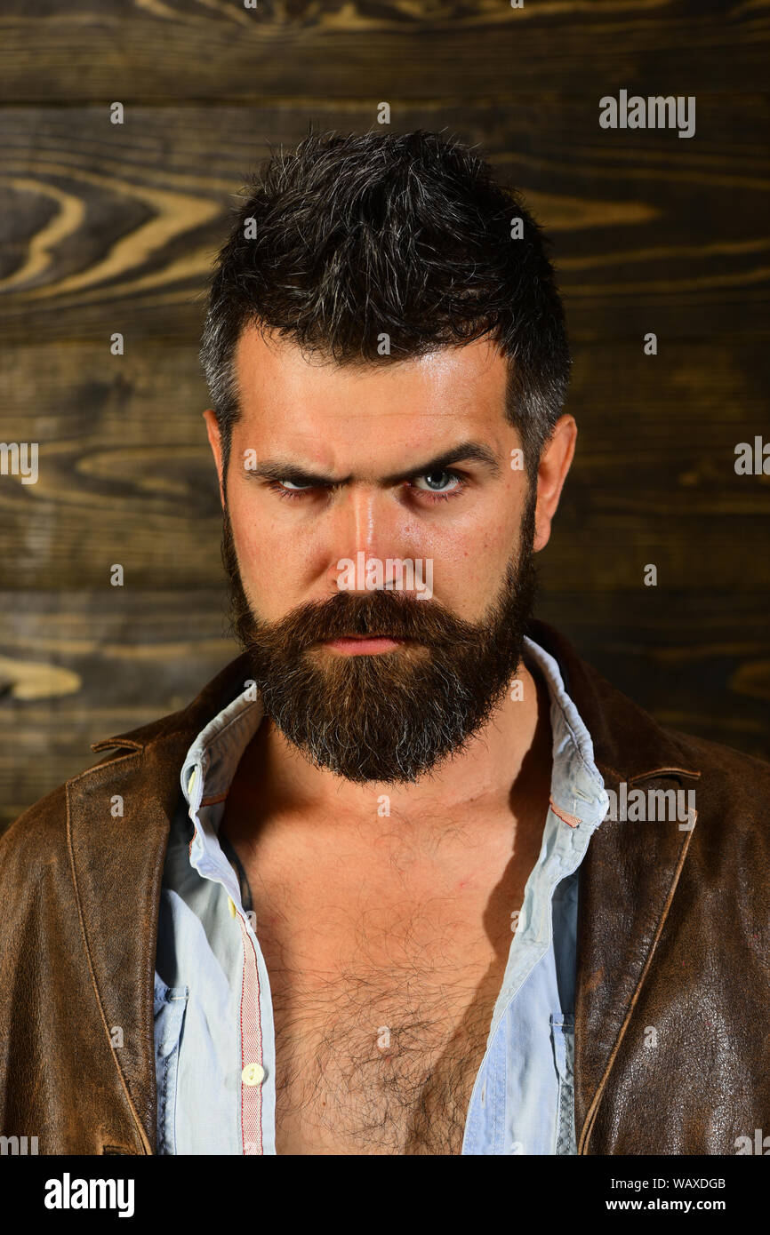 Hipster grave dans un barbier, look. Hipster avec barbe, visage sérieux sur fond de bois. Banque D'Images