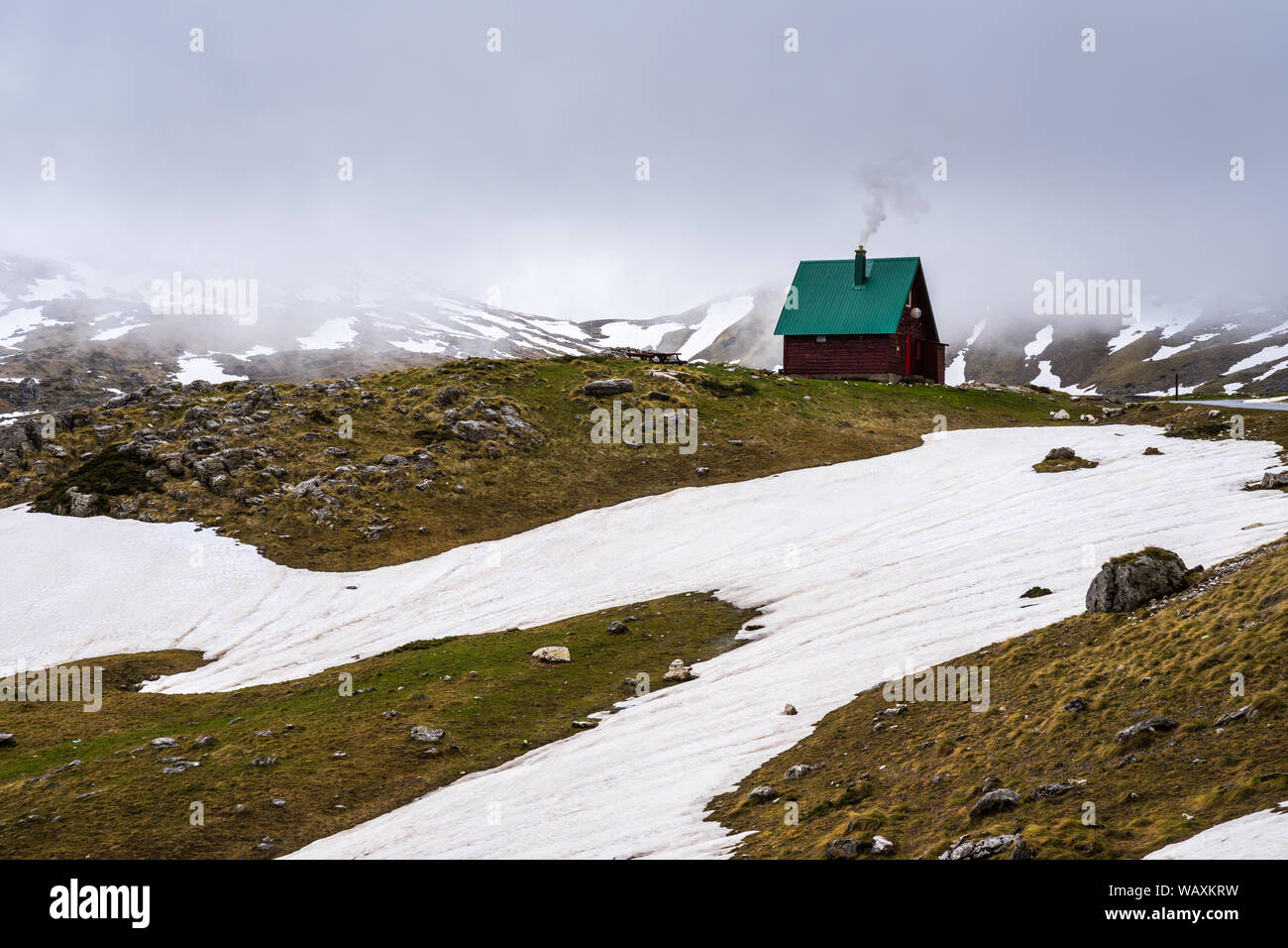 Le Monténégro, petit refuge de montagne en bois avec cheminée fumer dans la neige couverts nature paysage alpin à côté de la fonte des neiges à springtide sedlo col ro Banque D'Images