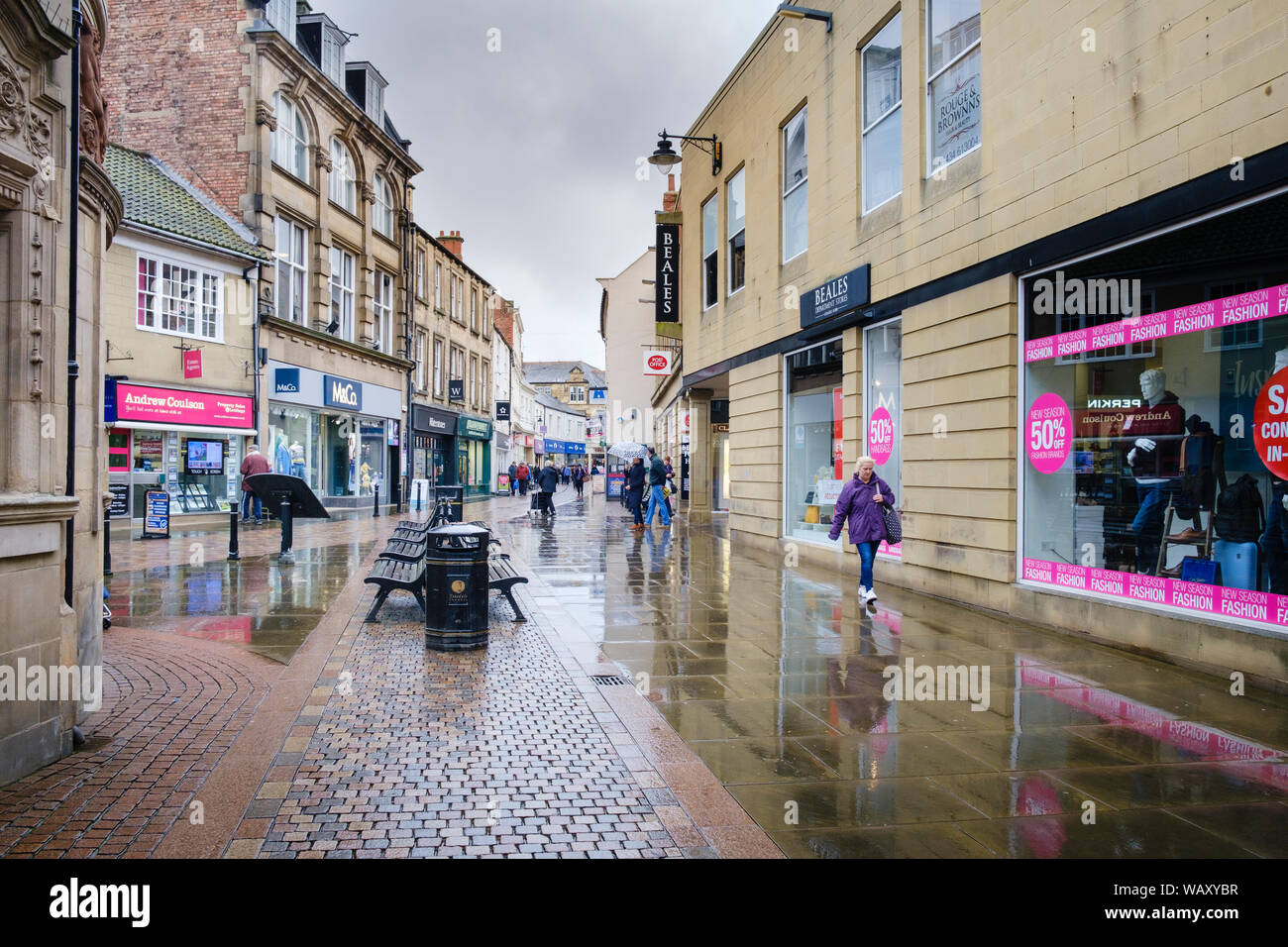 Clients dans une zone piétonne et commerçante dans la pluie, dans la rue avant de Northumberland Hexham Banque D'Images