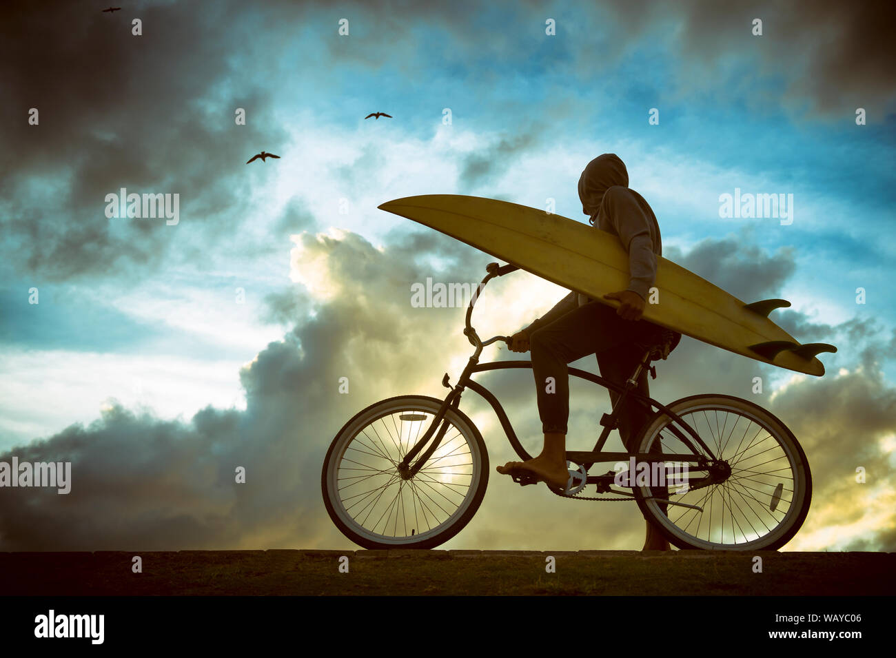 Silhouette de surfer carrying his surfboard sur une plage en vtt en face de ciel lumineux Banque D'Images