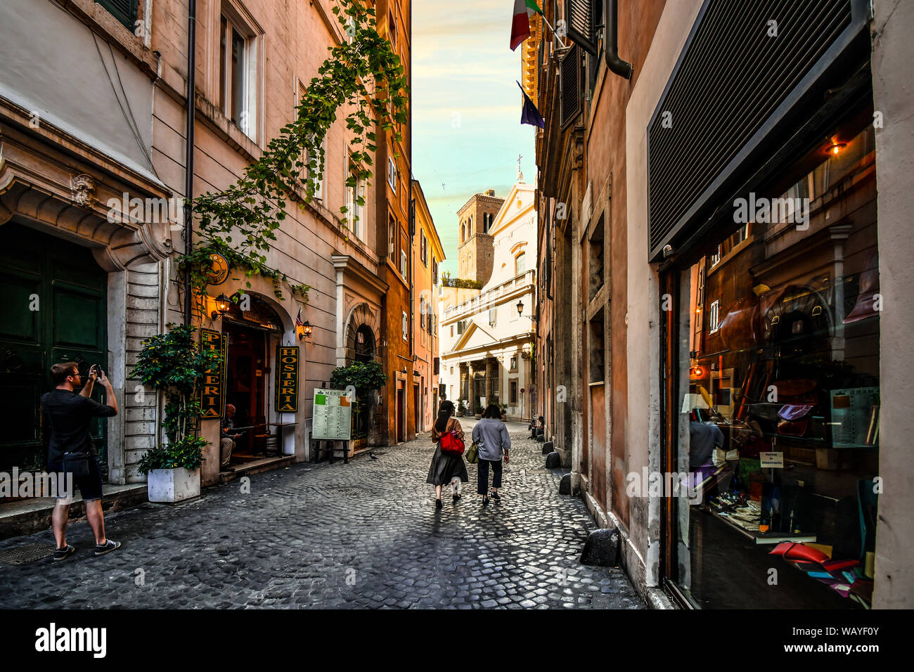Les touristes passent devant un magasins ruelle ombragée vers l'église Saint Eustache avec le cerf blanc sculpture sur le toit à Rome, Italie Banque D'Images