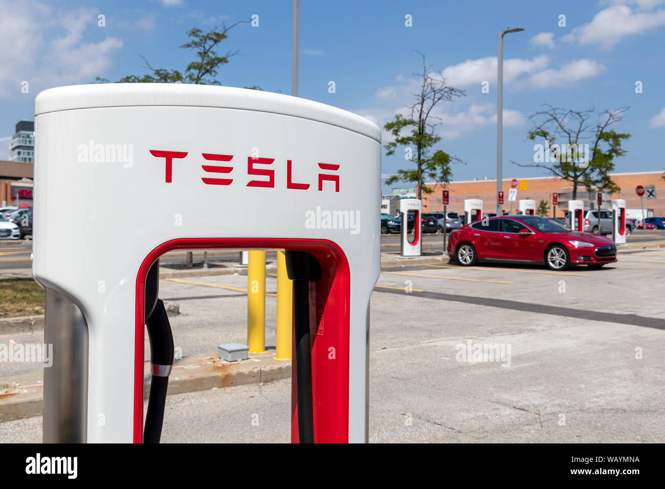 Logo texte Tesla tesla haut de Décrochage compresseur avec Tesla Model S rouge garée dans l'arrière-plan. Banque D'Images Logo texte Tesla tesla haut de Décrochage compresseur avec Tesla Model S rouge garée dans l'arrière-plan. Banque D'Images
