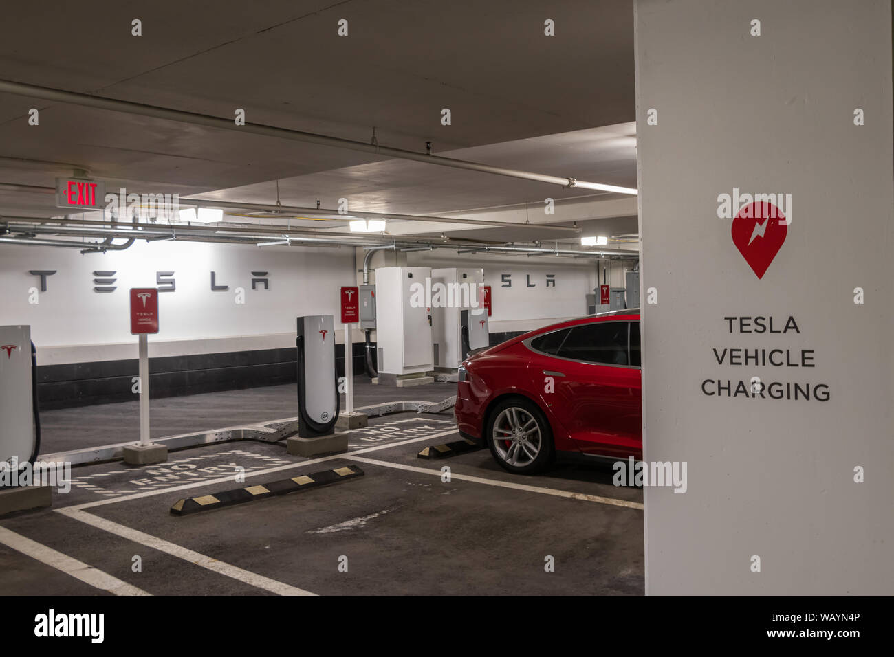 Recharge de véhicules Tesla signe sur un poste dans un garage de stationnement alors que la Model S Tesla Tesla au frais derrière la station de compresseur. Banque D'Images Recharge de véhicules Tesla signe sur un poste dans un garage de stationnement alors que la Model S Tesla Tesla au frais derrière la station de compresseur. Banque D'Images