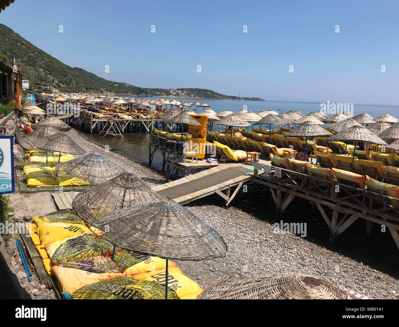 Plage avec chaises longues et parasols sur des pilotis au-dessus de l'eau dans le port d'Assos sur la côte égéenne de la Turquie. Banque D'Images