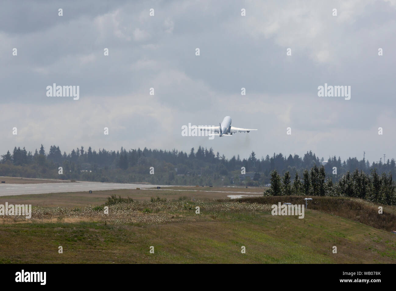 Un Dreamlifter décolle à Paine Field à Everett, Washington, le 22 août 2019. Le gros-cargo) est un Boeing 747-400 modifié utilisé pour le transport des composants du Boeing 787 Dreamliner. Dans la distance sont l'usine Boeing d'Everett, hangars de peinture où une majorité de ses avions à fuselage large sont peintes avant le dernier vol test. Banque D'Images