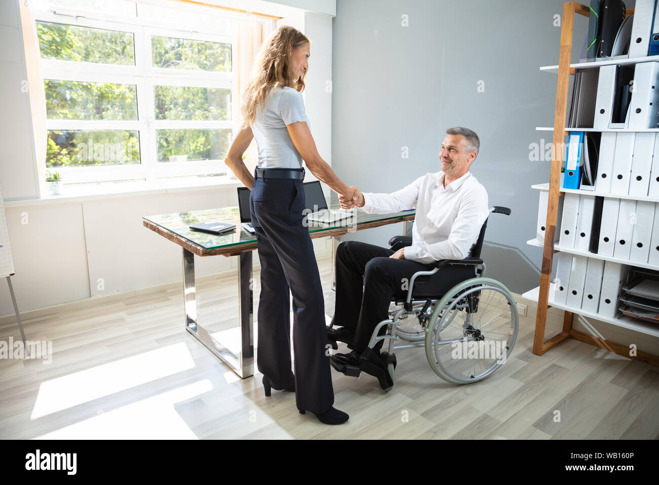 Professionnels Mobilité Businessman Sitting on Wheelchair Shaking Hand avec son partenaire in Modern Office Banque D'Images
