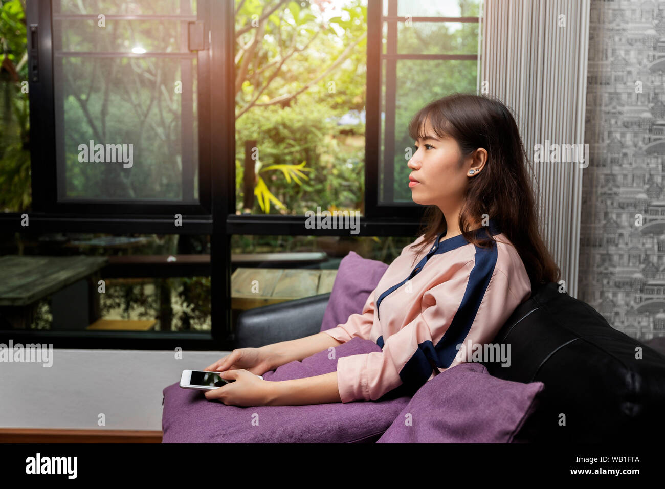 Beautiful Young Asian woman using mobile phone while sitting on sofa Banque D'Images
