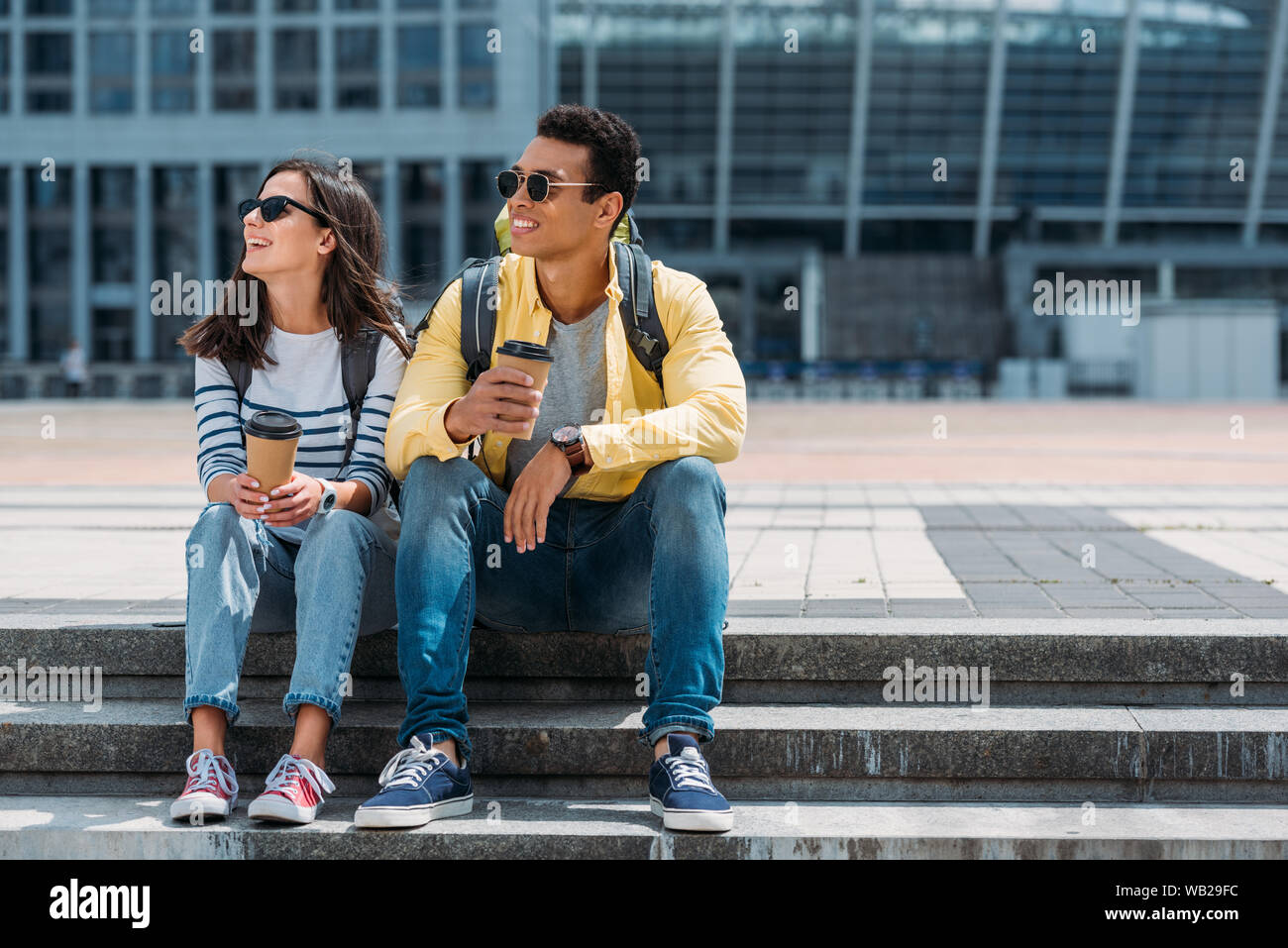 L'Interracial les touristes avec des sacs à dos assis dans les escaliers avec du papier de tasses de café et à l'écart Banque D'Images