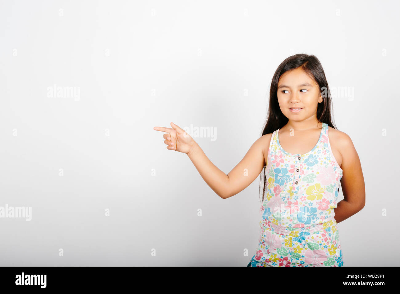 Une fillette de 9 ans est dirigé vers son côté gauche. Elle est debout devant un mur blanc. Elle est souriante. Elle a de longs cheveux noirs. Elle a d'interieurélectronique hispanique Banque D'Images