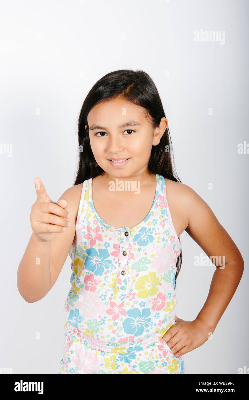 Une fillette de 9 ans est dirigé vers l'appareil photo. Elle est debout devant un mur blanc. Elle est souriante. Elle a de longs cheveux noirs. Elle a les caractéristiques d'origine hispanique. Sh Banque D'Images