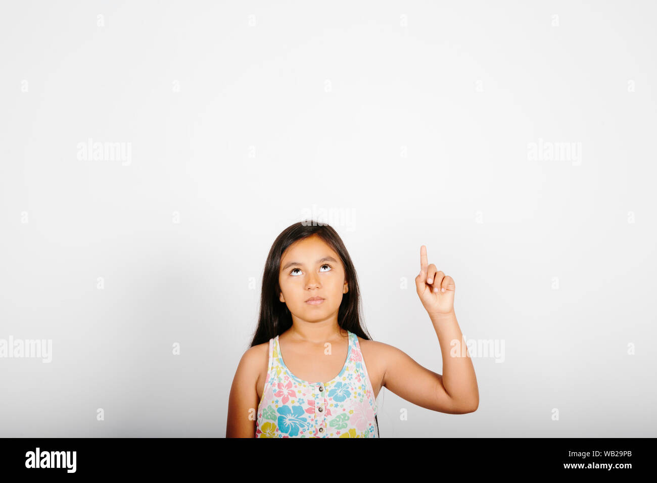 Une fillette de 9 ans est dirigé vers son côté droit. Elle est debout devant un mur blanc. Elle est souriante. Elle a de longs cheveux noirs. Elle a hispanic feat Banque D'Images
