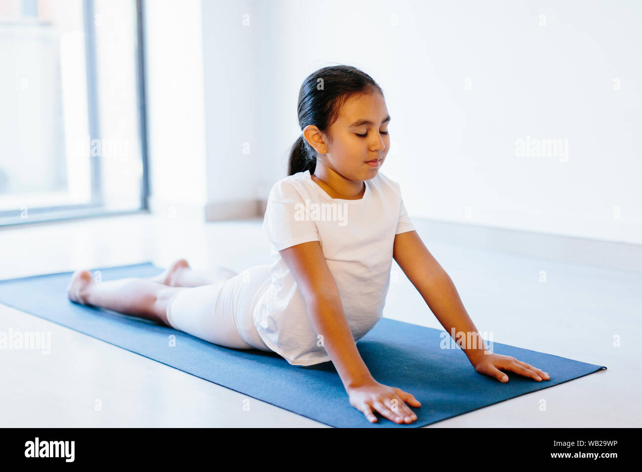 Une fillette de 9 ans fait yoga pose allongé sur un tapis de yoga. Elle portait des vêtements blancs. Elle a l'ethnicité hispanique caractéristiques. Banque D'Images