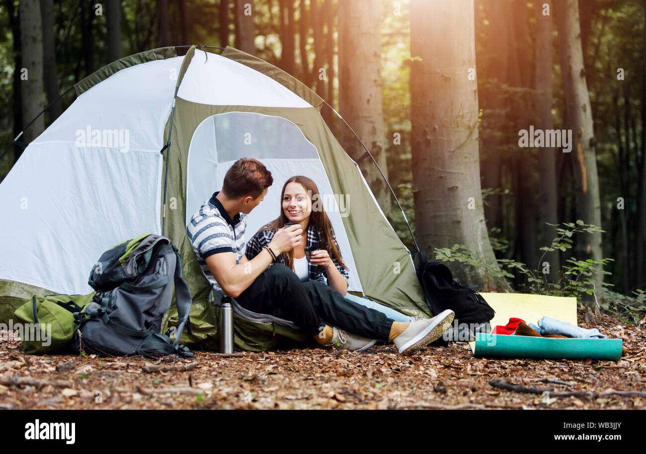 L'homme et la femme les randonneurs se reposer en face de la tente à forêt sous ciel sur fond de forêt Banque D'Images