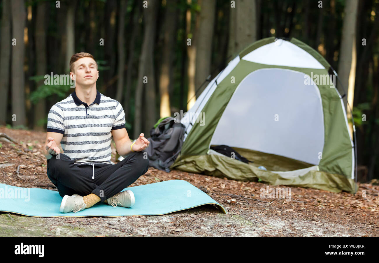 Les jeunes bel homme médite près de la tente à la forêt Banque D'Images