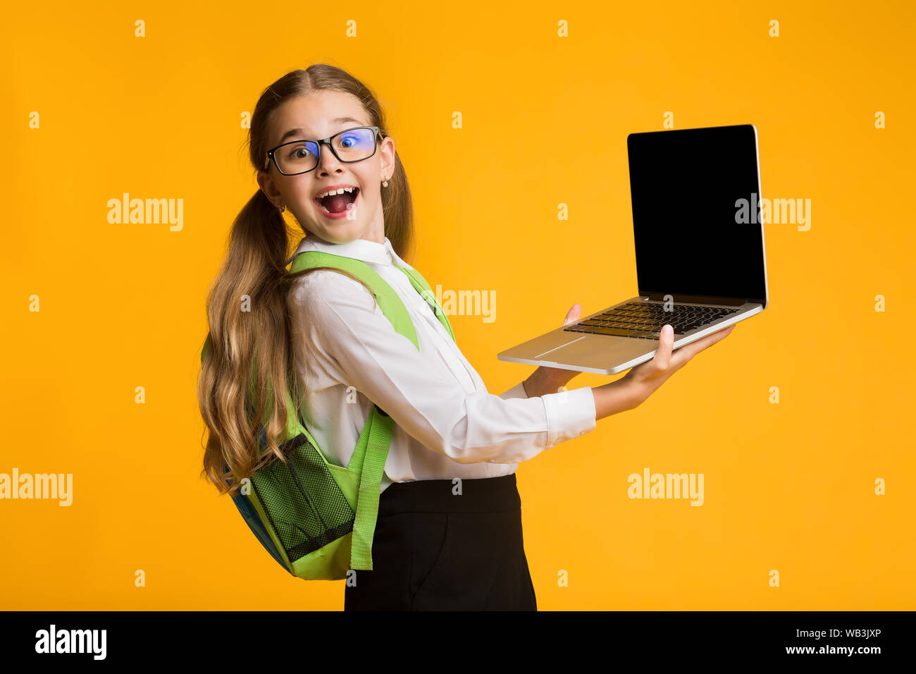 Happy Schoolgirl Holding Laptop avec écran noir sur fond jaune Banque D'Images
