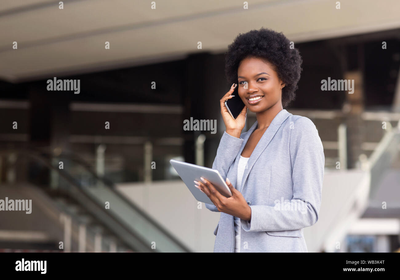 Jeune femme parlant au téléphone cellulaire, à l'aide de tablette numérique près de l'immeuble de bureaux modernes Banque D'Images