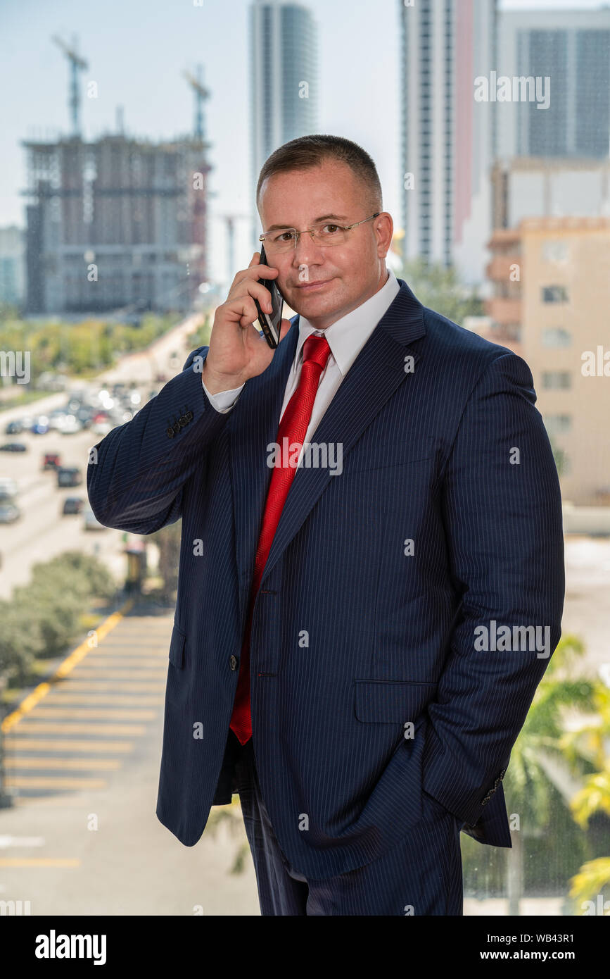 Portrait o fa senior caucasian businessman standing par une fenêtre de son bureau tout en parlant au téléphone et regardant la caméra Banque D'Images