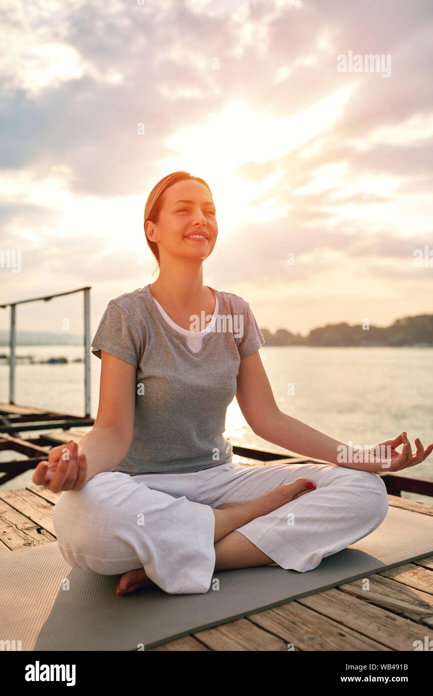 Belle femelle sur dock méditer en yoga pose par river Banque D'Images