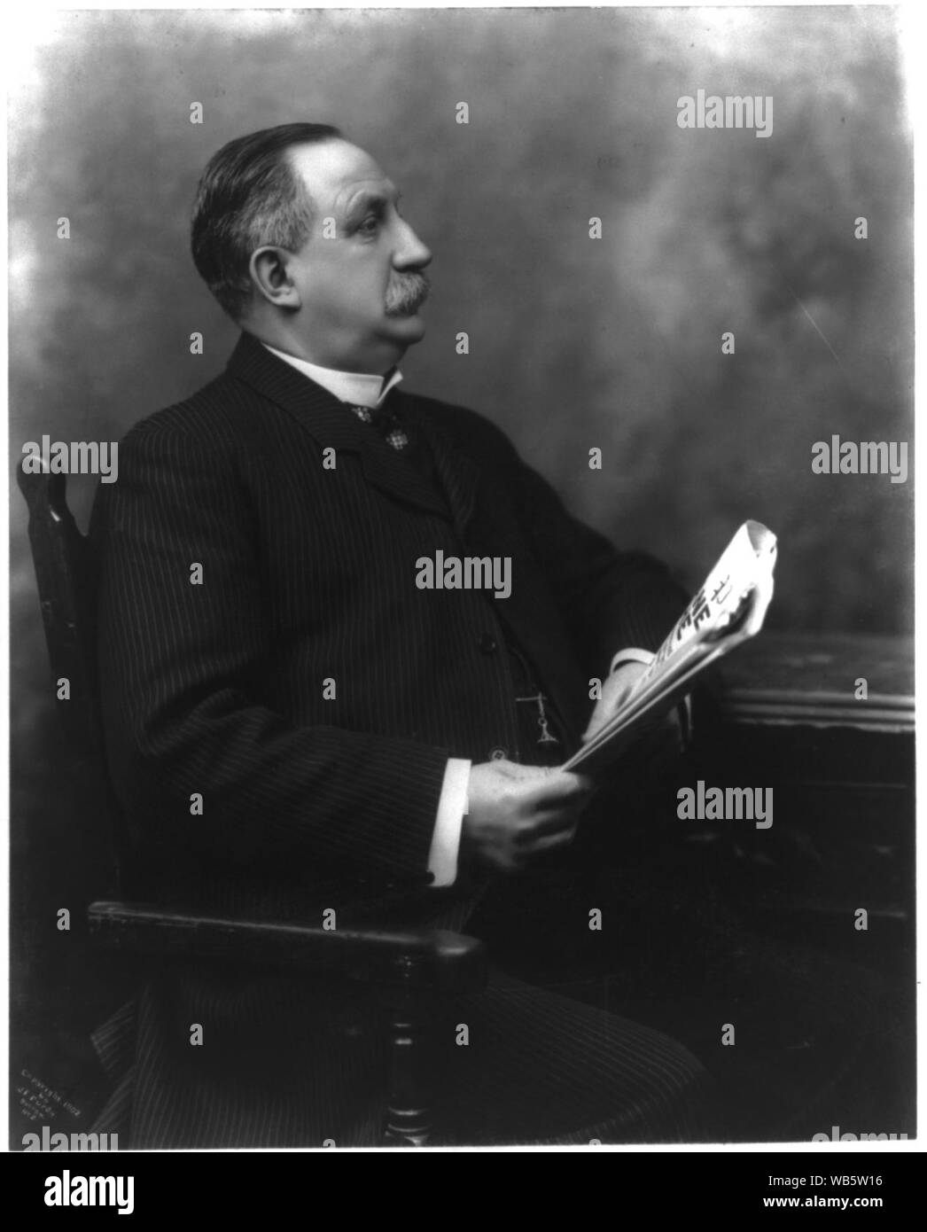 E.P. Shaw, longueur de trois quarts, assis, holding newspaper Banque D'Images