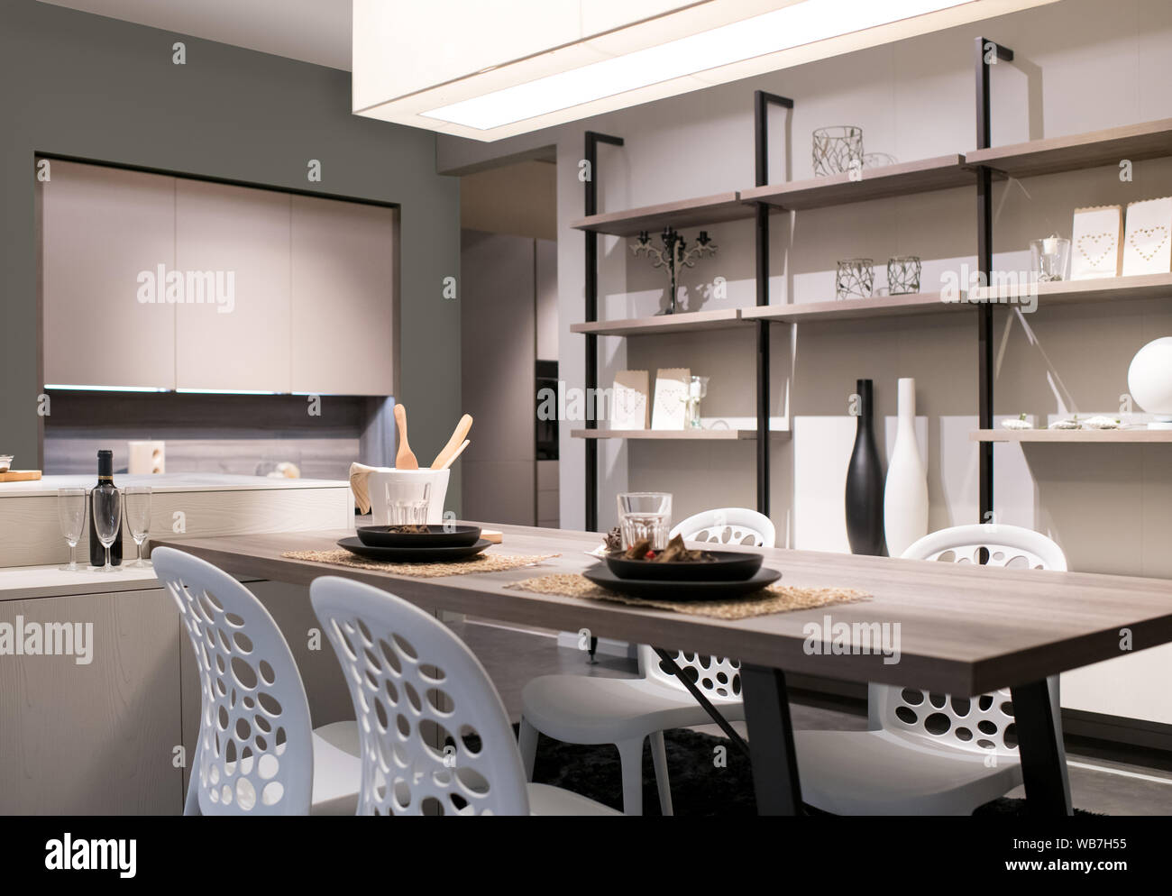 Cuisine ouverte et salle à manger avec un décor beige neutre, unité murale étagères et une table et chaises moderne éclairé par une grande lumière au plafond Banque D'Images