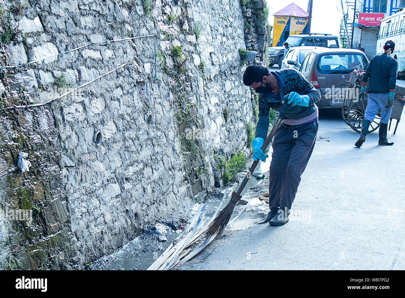 Shimla, Himachal Pradesh, Inde - Juillet 20th, 2019 : employé municipal balayer le système routier et de drainage avec balai et collecte des déchets, assainissement worke Banque D'Images