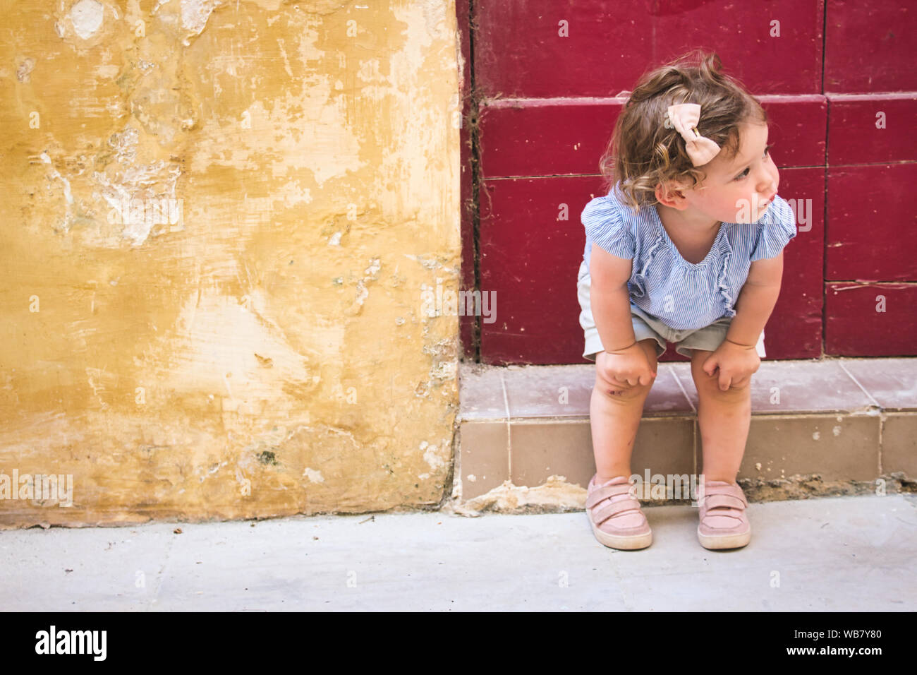 Cute baby girl sitting on la porte d'un village rural home Banque D'Images