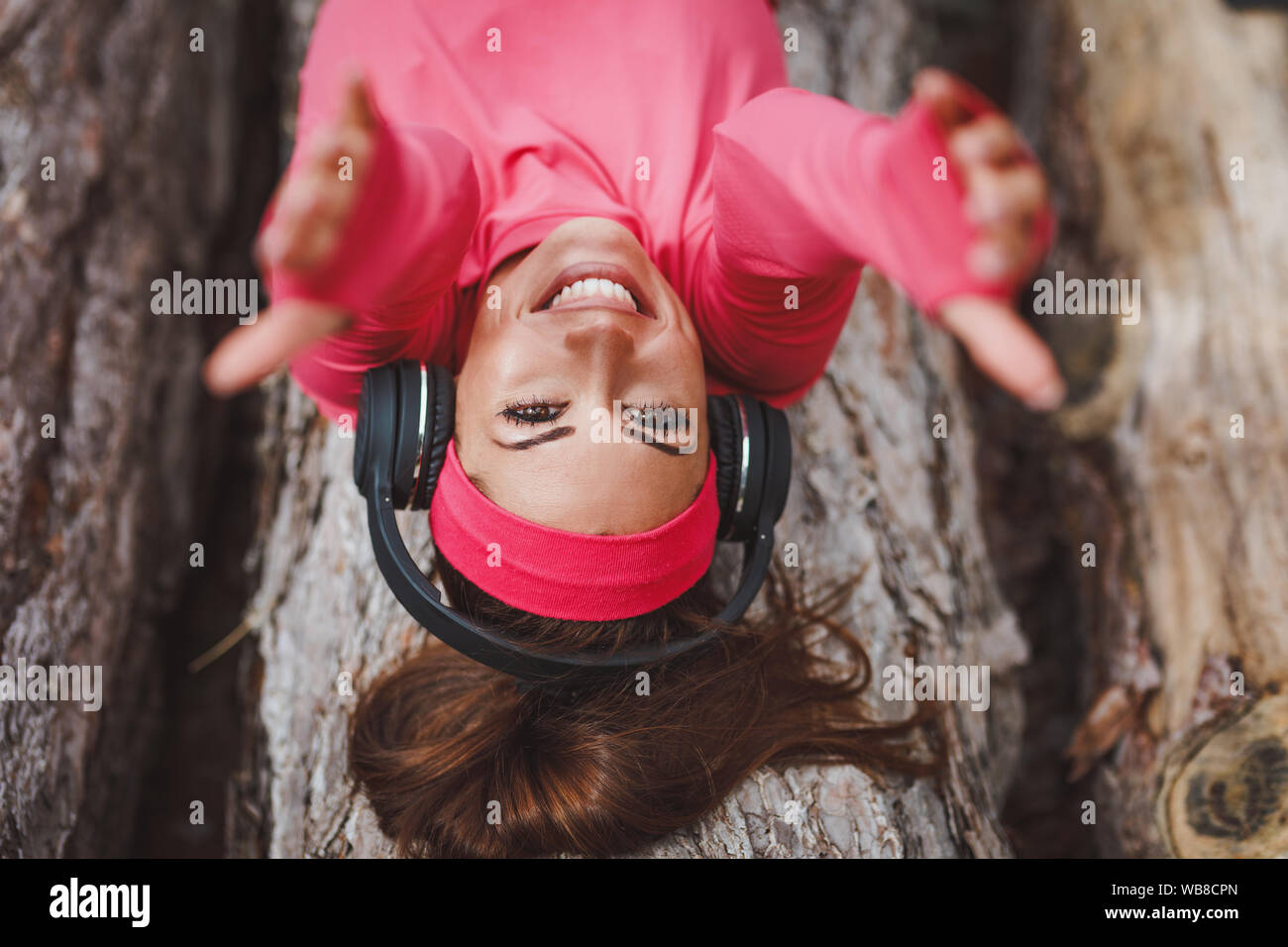 Young female runner couché sur un journal en bois et faire une pause avec la musique après une marche en forêt. Elle est donne à ses mains comme s'appeler quelqu'un à Banque D'Images