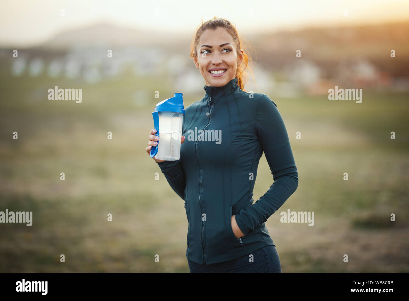 Young beautiful smiling female runner est l'eau potable et la préparation à la course en montagne. Banque D'Images