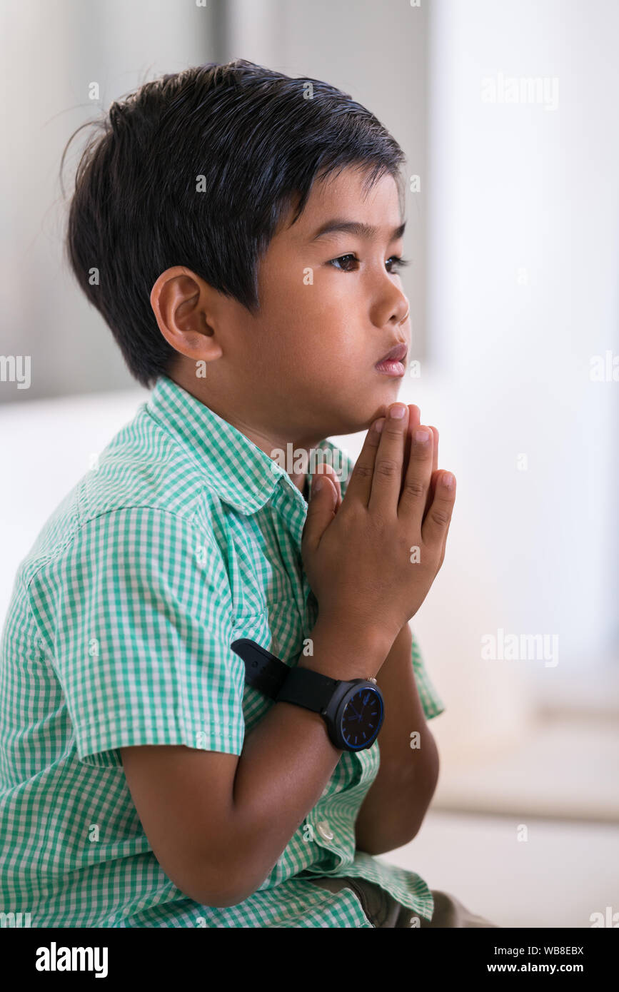 Mixed Race jeune garçon tient ses mains en prière et assis sur la chaise Banque D'Images