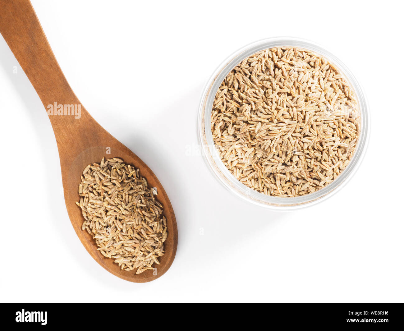 Les graines de cumin (Cuminum Jeera), dans une tasse en verre et cuillère en bois sur fond blanc Banque D'Images