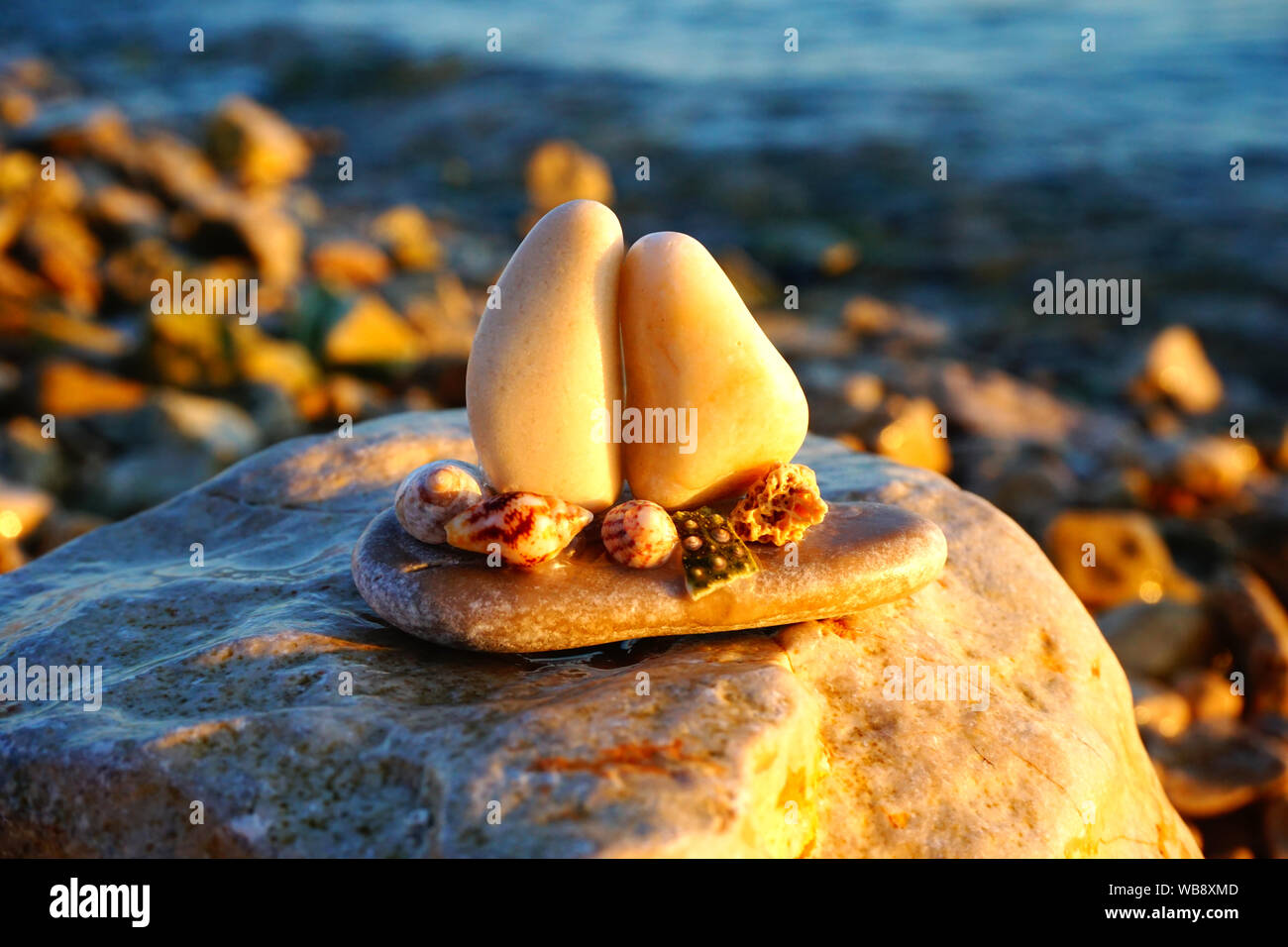 Les arts et la nature et de galets de fond marin avec petit bateau fabriqué à partir de cailloux et des coquillages sur la plage de galets au coucher du soleil Banque D'Images
