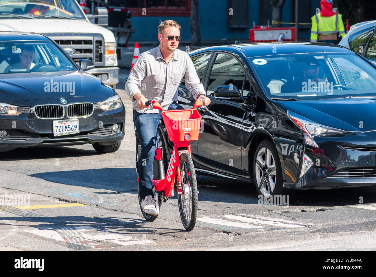 21 août 2019 San Francisco / CA / USA - Man riding un saut vélo électrique ; sur la droite une voiture avec le super sticker peut être vu ; JUMP est un dockless Banque D'Images