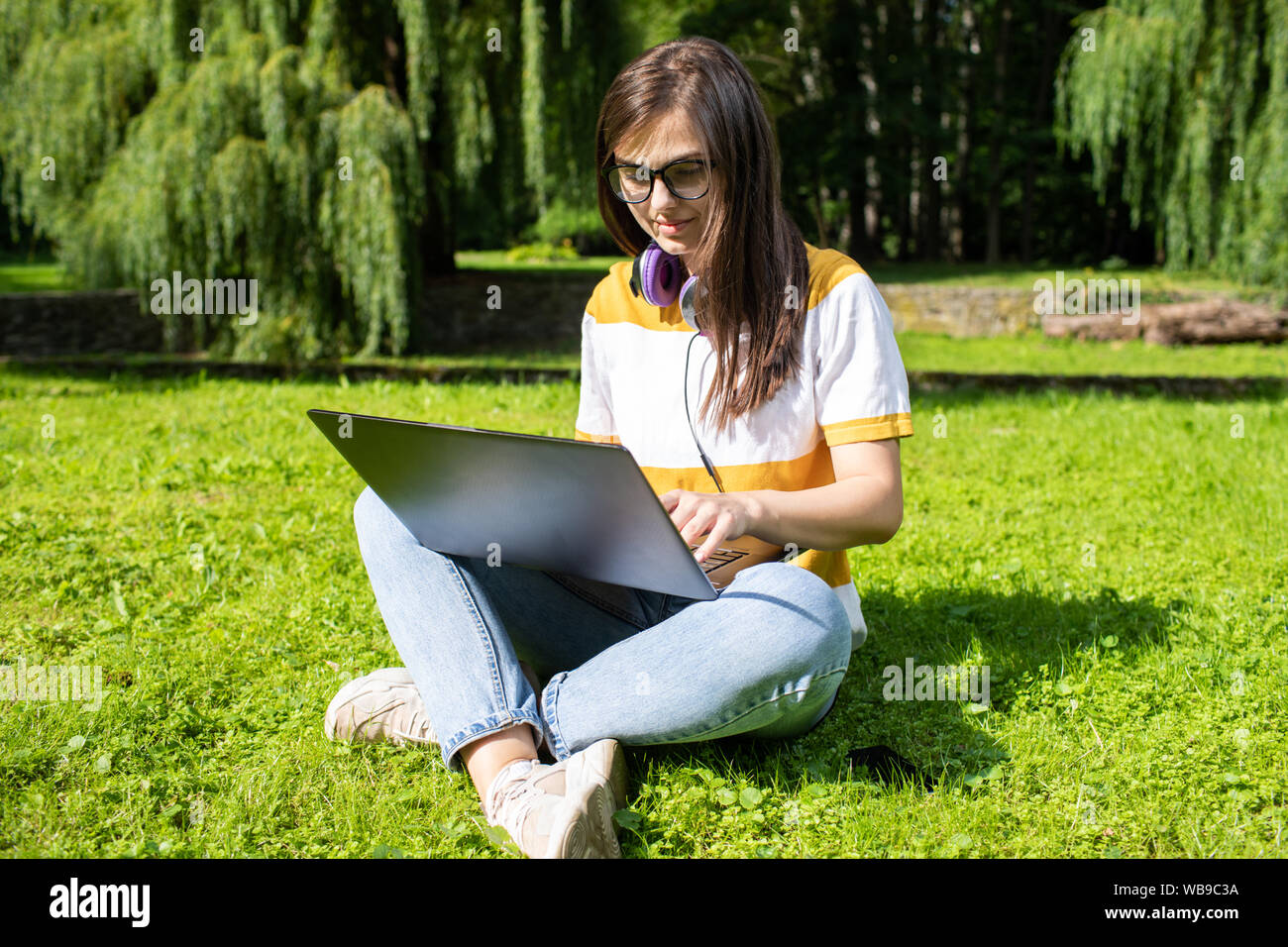 Belle jeune brunette woman with laptop sitting on park lawn Banque D'Images