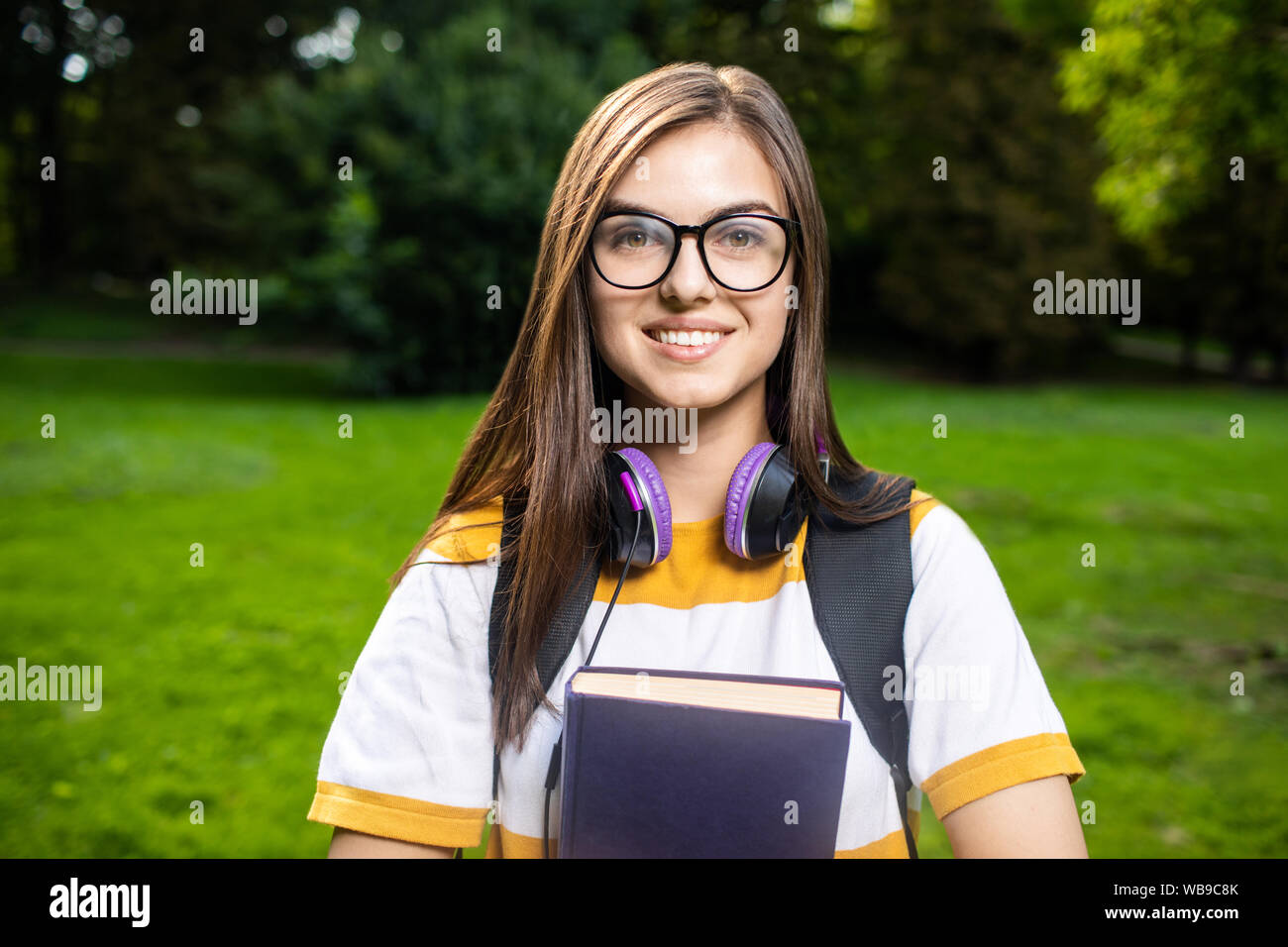 Portrait of smiling student girl avec daypack et books in park Banque D'Images