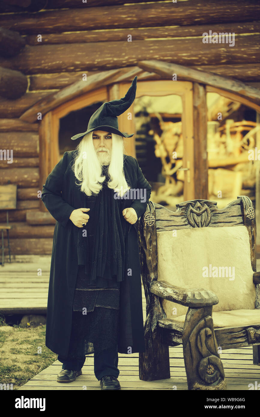 Homme mauvais magicien à longs cheveux gris barbe en costume noir et  chapeau pour l'Halloween à l'extérieur sur l'arrière-plan maison Photo  Stock - Alamy