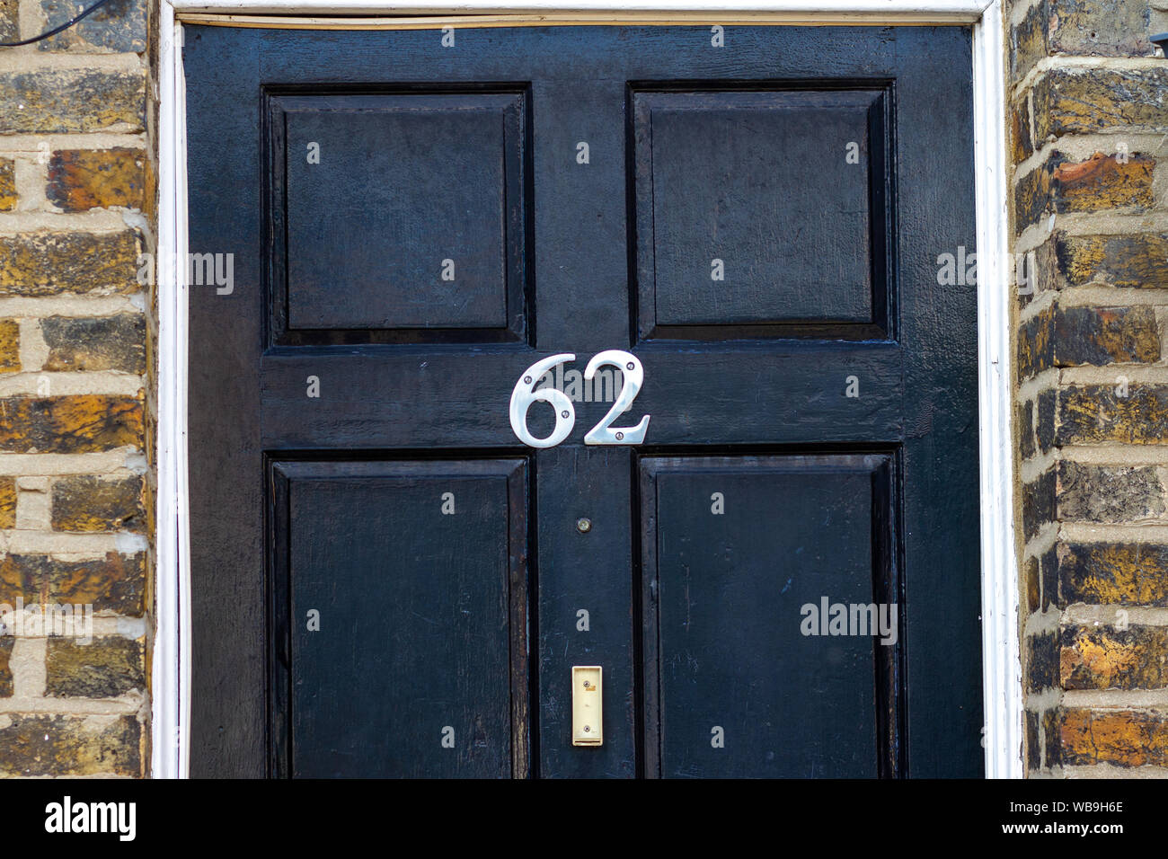 Numéro de maison 62 sur une porte avant en bois noir avec cadre en brique environnante Banque D'Images