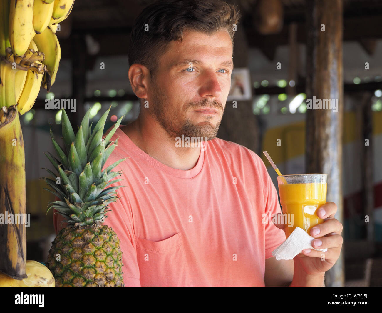 Un homme vêtu de vêtements à la mode se trouve dans un café au bord de l'océan tropical, des boissons de jus de mangue naturelle. L'heure d'été. Banque D'Images