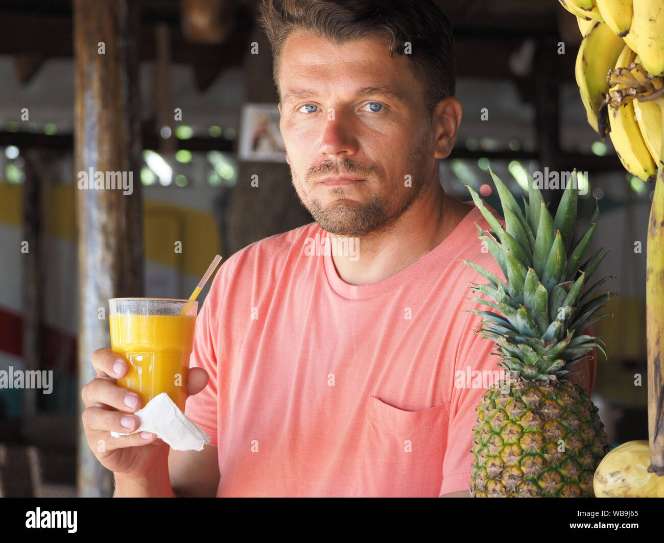 Un homme vêtu de vêtements à la mode se trouve dans un café au bord de l'océan tropical, des boissons de jus de mangue naturelle. L'heure d'été. Banque D'Images