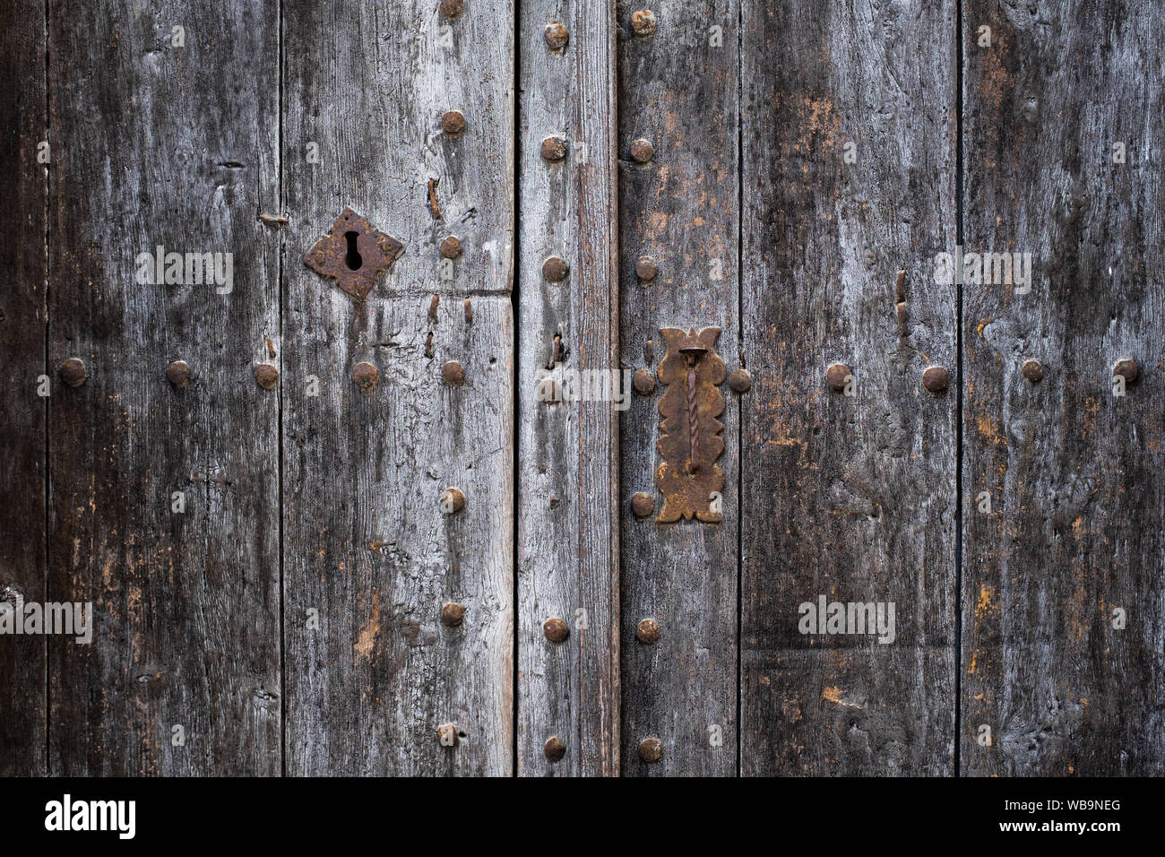 Porte en bois ancien espagnol : poignée rouillée, verrouillage et rivets. La surface rugueuse du bois gris avec motif de fond fissuré. Banque D'Images