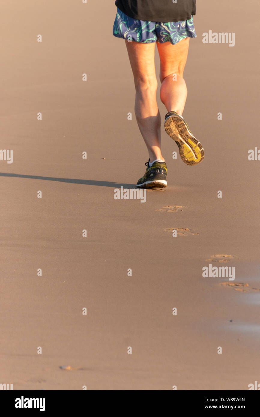 Une vue arrière d'un runner femmes faire son jogging sur la plage Banque D'Images