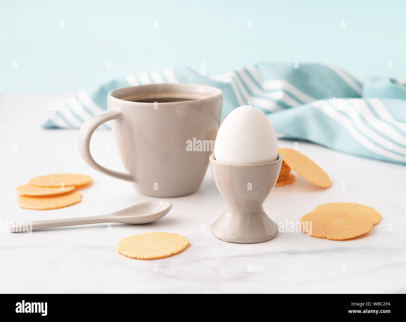Oeuf dur en céramique egg cup, tasse de café et les croustilles de maïs mince et croustillante sur fond de cuisine turquoise serviette. Le petit-déjeuner gratuit. Copier l'espace. Banque D'Images