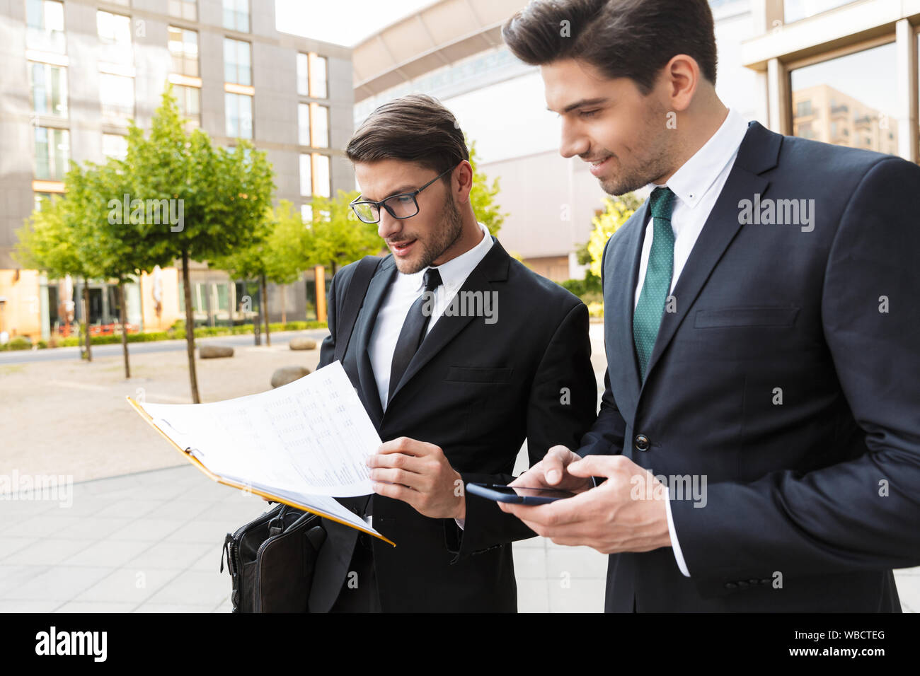 Deux beaux jeunes hommes d'assurance convient de porter à l'extérieur à l'article les rues de la ville, discuter de nouveau projet, holding clipboard Banque D'Images