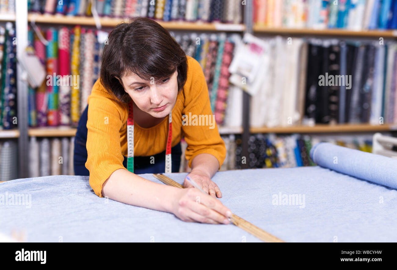 Vendeuse compétente a ordonné de mesure pour la coupe de tissu textile en boutique, la préparation pour la vente Banque D'Images