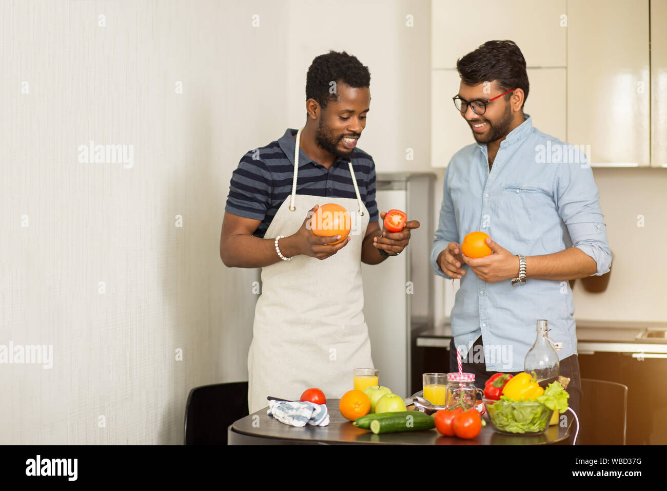 Deux beaux mâles joyeux amis debout dans la cuisine de fruits dans les mains, parler, faire du jus d'orange et de pamplemousse, la préparation des aliments sains t Banque D'Images