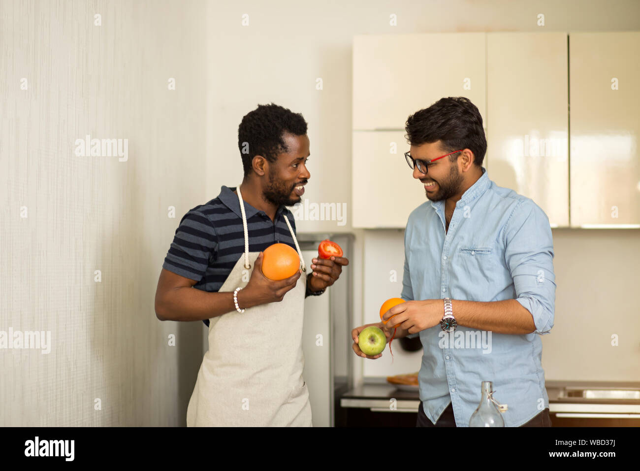 Deux garçons de vêtements décontractés pour aller dans la cuisine cuisine smoothie article de hostel, holding pamplemousse, orange, pomme, tomate en mains, cheer Banque D'Images